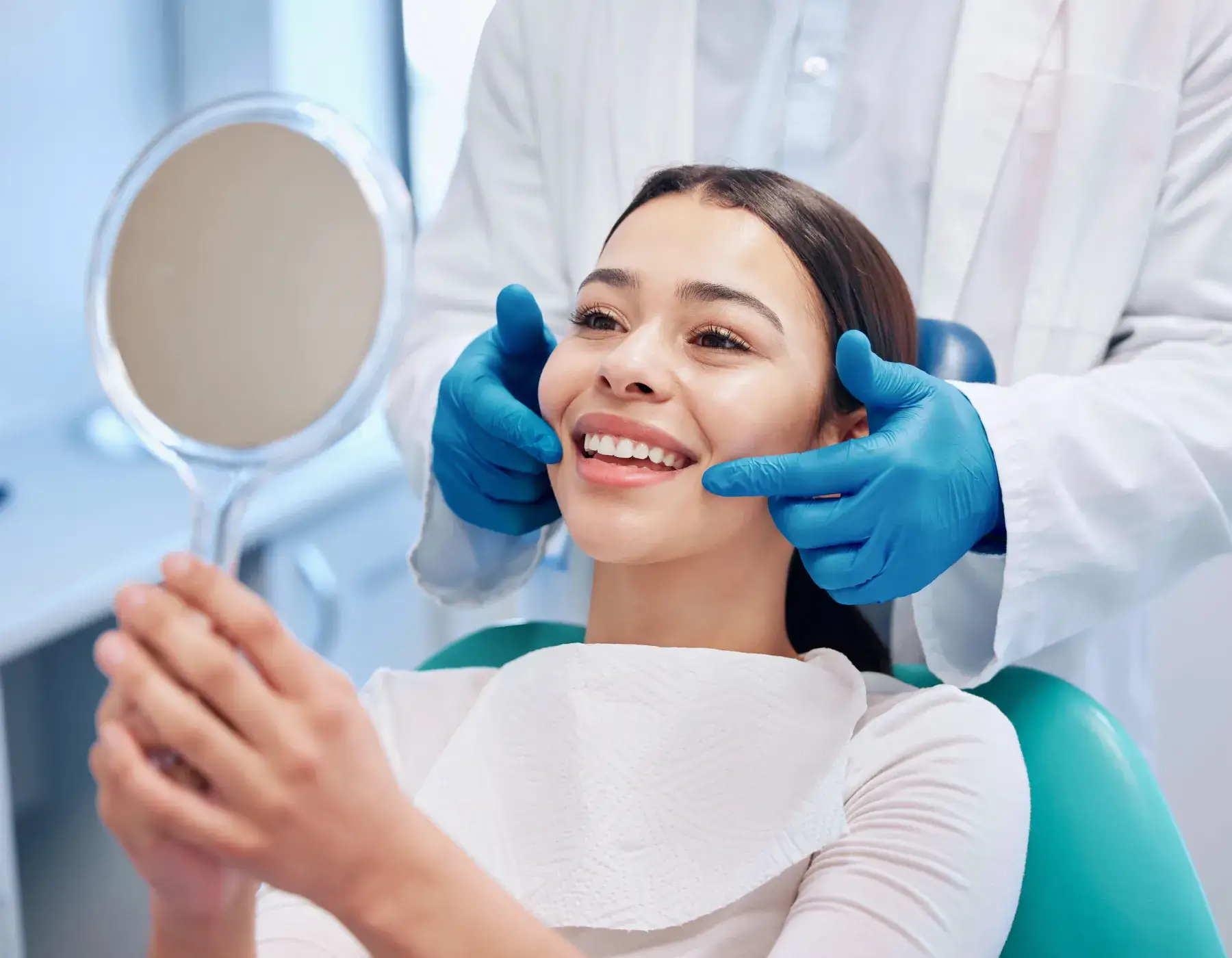 A dentist helps a smiling patient check her teeth in a handheld mirror.