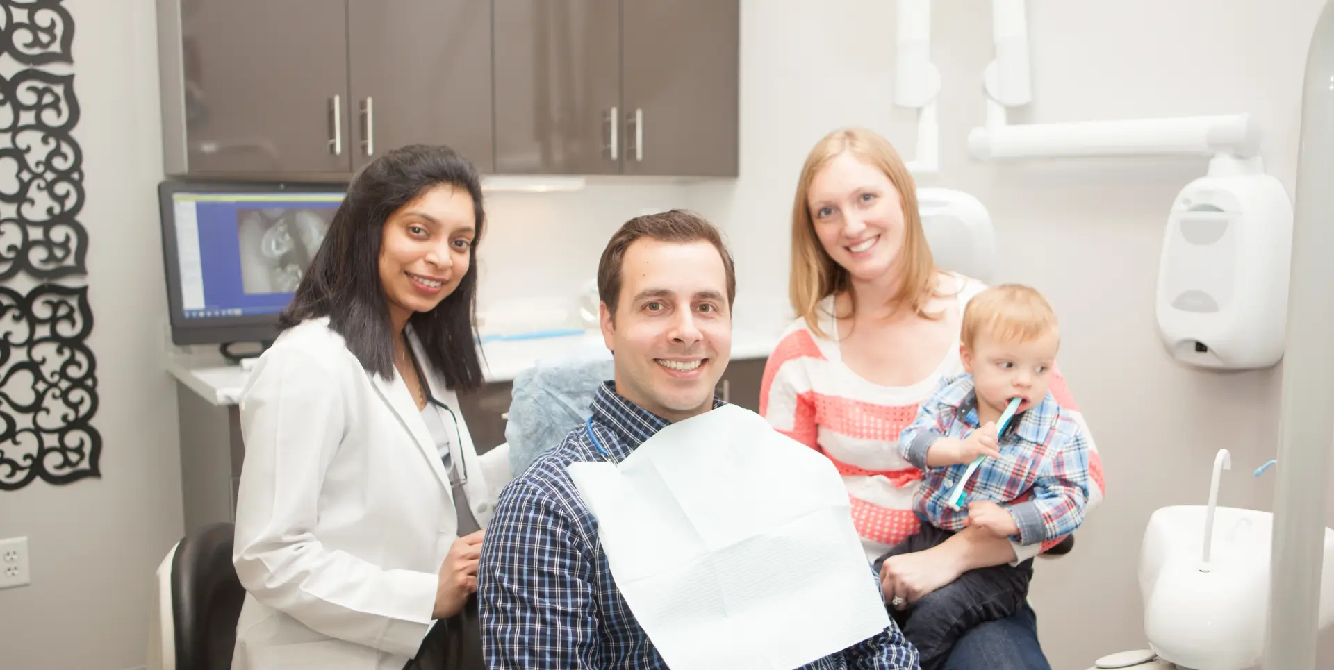 Dentist and patient smiling for a photo, with a mother holding her child nearby.